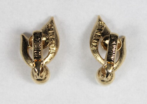 Back of two gold toned plated metal clip-on earrings, with the Sarah Coventry mark on the back of the clip on each earring.