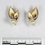 Front of two gold toned metal earrings with each earring consisting of a faux pearl and two leaf-shaped elements, and a black and white 5 cm scale.