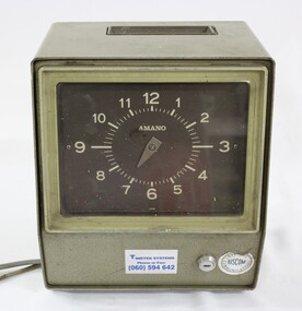 Green metal time clock with a brown clock face and light coloured numbers. Two labels attached to the lower front surface with a horizontal lock between them and electrical cords extending from one side. 