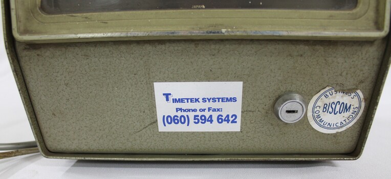 Detail of the two labels and horizontal lock on the lower front surface of the Amano time clock.