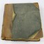 Front of a bound ledger with a deteriorated light brown leather and green textile cover.