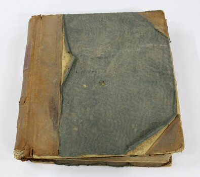Front of a bound ledger with a deteriorated light brown leather and green textile cover.