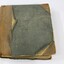 Front of a bound ledger with a deteriorated light brown leather and green textile cover, with a black and white 5 cm scale.