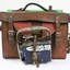 Front of a Victorian Railways guard's satchel, with a dark blue metal lamp attached to the front and rolled up green signal flag attached to the top.