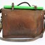 Back view of a Victorian Railways guard's satchel, with a rolled up green signal flag attached to the top amd a brass padlock on the proper left side.