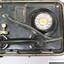 Lower part of a metal case containing a black rotary dial flameproof telephone, with rubber tubing attached to the handset and a metal plate with the maker's name and the type and certification of the telephone, with a black and white 10 cm scale.