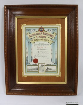 Dark brown wooden frame on a colour certificate for past officers in the Wodonga sub-branch of the Victorian Branch of the Australian Railways Union, with a black and white 10 cm scale.
