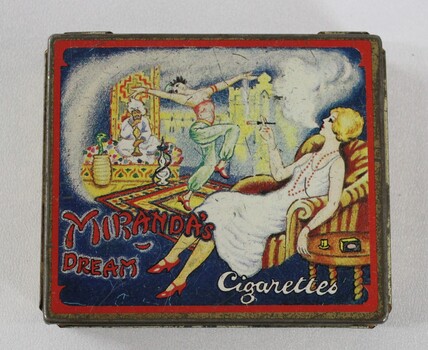 A tobacco tin with a coloured illustration of a woman in stylish 1920s-1930s dress sitting in an armchair smoking a cigarette, while watching an Orientalist scene featuring a belly dancer and a snake charmer wearing a turban. 