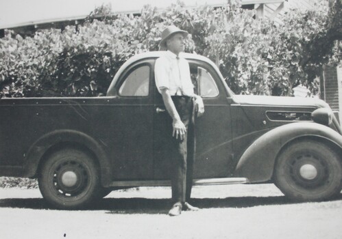 Black and white photograph of man standing beside a 1930s ute 