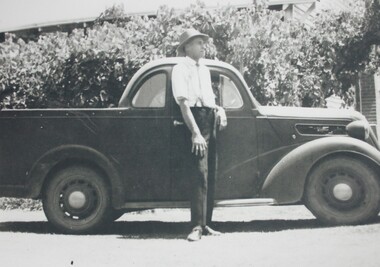 Black and white photograph of man standing beside a 1930s ute 