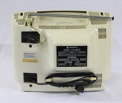 Back of the Sanyo colour television with the electric cable wrapped around the bottom, a plastic cable connected to the antenna, and  three labels with the serial number and safety warnings. 