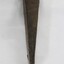 Side view of a hand forged iron alloy wedge with a cracked flange/rim at the top, red-brown rust and some dirt on the surface.