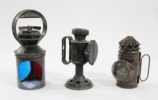 Three metal and glass lamps, one with blue and red filters, used for signalling on the Victorian Railways.