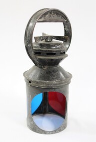 Exterior casing of a black painted metal railway signal lamp with circular blue and red glass filters and a turning mechanism on the top under a circular handle.