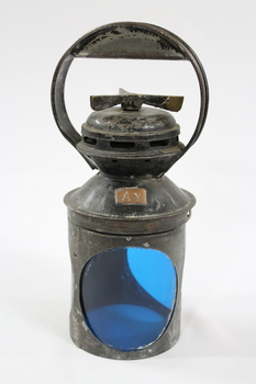 Exterior casing of a black painted metal railway signal lamp with "A y" stamped on a small copper plate on one side, as well as a circular blue glass filters and a turning mechanism on the top under a circular handle.