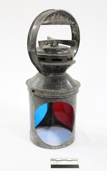 Exterior casing of a black painted metal railway signal lamp with circular blue and red glass filters and a turning mechanism on the top under a circular handle.