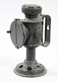 Side view of a black painted metal signal lamp with a circular metal cover over a glass disk at the front. The circular metal cover has a vertical slit in it.