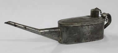 Proper left side of a grey metal container with a long spout, handle and a chain attached to the lid.