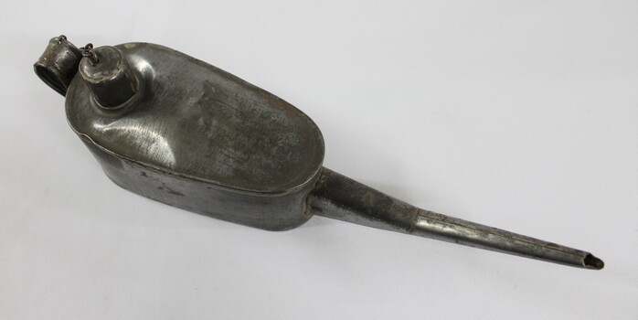 View from above of a grey metal container with a long spout, handle and a chain attached to the lid.