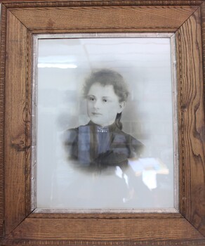 Black and white photographic portrait of a woman in a black, early 20th dress, in a thick wooden frame