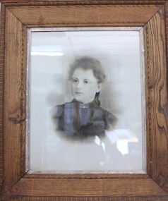 Black and white photographic portrait of a woman in a black, early 20th dress, in a thick wooden frame