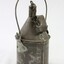 Back of a grey metal container with a looped handle attached to the sides, as well as a handle on the back of the container with a metal chain attached to it to secure the cap for the container. 