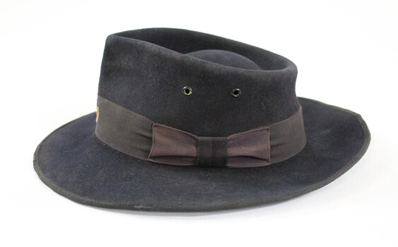 Proper left side of a dark blue/grey felt Victorian Railways hat with a faded brown band and trim..