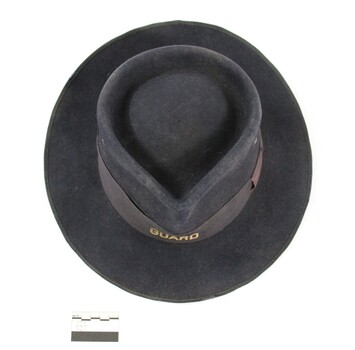 Dark blue/grey felt Victorian Railways hat with the word 'GUARD' in gold on the front of a faded brown band and a black and white 5 cm scale.