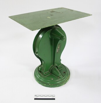 Back view of the green painted cast iron scales with a flat rectangular surface for weighing up to 25 kg, with a black and white 10 cm scale to indicate the size of the scales.
