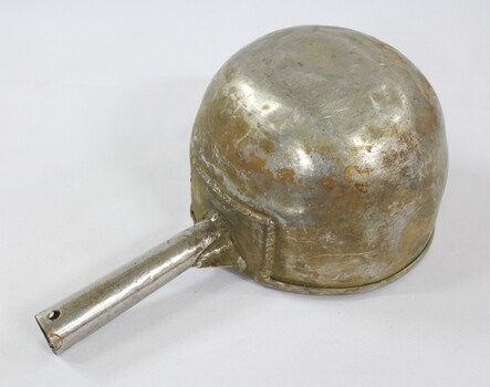 Underside of a large aluminium scoop with a handle soldered on one side edge.
