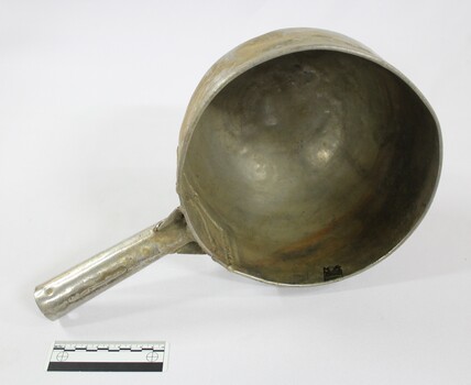 Large aluminium scoop with a handle soldered on one side edge and a black and white 10 cm scale.
