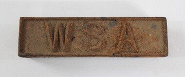 Rectangular corroded cast  iron identification tag with the letters '"WSA" on the upper surface.