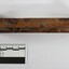 Side view of a rectangular corroded cast  iron identification tag with a black and white 5 cm scale.