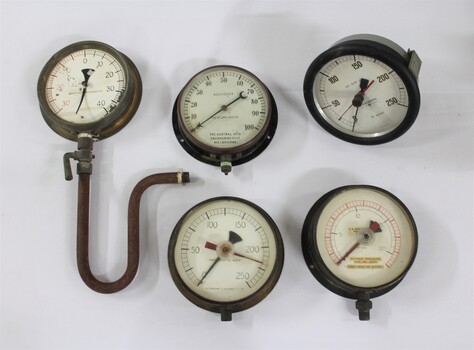 Five metal and glass water pump pressure gauges, including one with a U-shaped pipe and lever attached. 