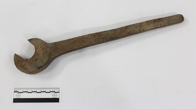 Large cast iron spanner with some ed/brown rust corrosion and light brown surface dirt. Black and white 10 cm scale in the foreground.