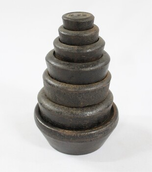 Set of seven metal weights with imperial measurements stacked from 4 oz. at the top to 7 lb. at  the bottom. 