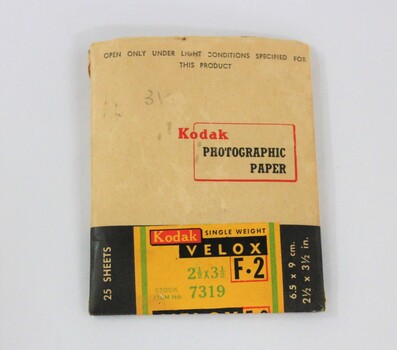A paper packet coloured light tan, black green, yellow and red, containing Kodak photographic paper.