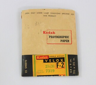 A paper packet coloured light tan, black green, yellow and red, containing Kodak photographic paper.