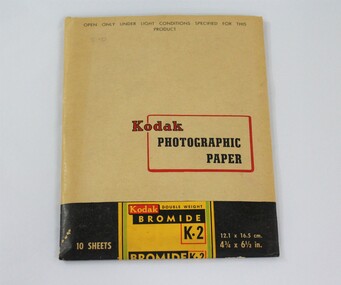 A paper packet coloured light tan, black green, yellow and red, containing Kodak photographic paper.