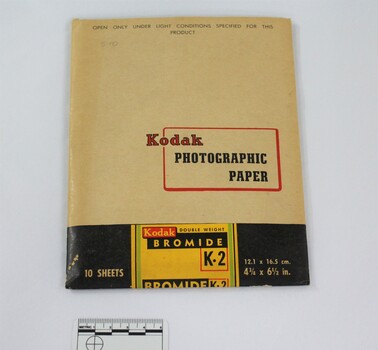 A paper packet coloured light tan, black green, yellow and red, containing Kodak photographic paper with 5cm scale