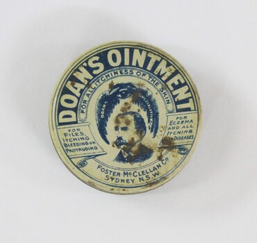 A round tin with branding and manufacturers information, and an illustration of man with a moustache. 