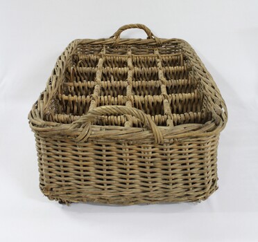 Narrow end of a rectangular wicker crate for delivering bottled drinks with 12 compartments and handles at each end.