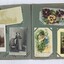 An open photograph album showing three black and white photographs and coloured greeting cards