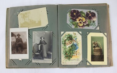 An open photograph album showing three black and white photographs and coloured greeting cards