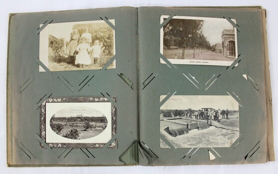 An open photograph album showing a black and white photograph and three postcards.