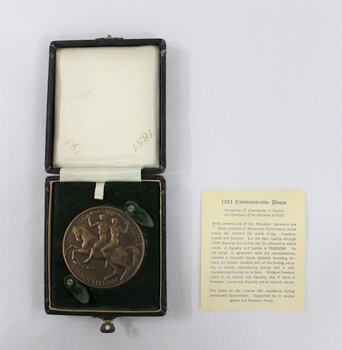 Circular bronze medal depicting a man and a woman riding a horse, in a small presentation box with a dark green velvet insert for the medal in the lower part and a light coloured textile printed with the dates 1851 and 1951 in the lid. Text on paper with a description of the medal next to the case.