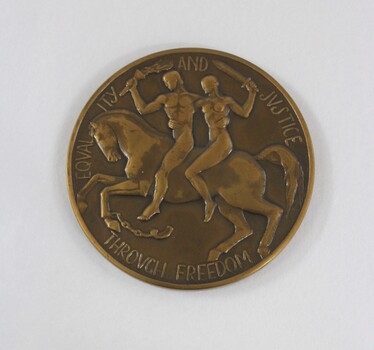 Obverse/front of a circular bronze medal depicting a man and a woman riding a horse, and the words "EQUALITY AND JUSTICE / THROUGH FREEDOM" in raised letters around the edge.