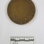 Reverse of a circular bronze medal with a stake surrounded by Australian floral motifs in the lower part and the words "CENTENARY OF THE GOVERNMENT OF VICTORIA 1851-1951" in raised letters around the top edge, and "Preseneted to / The Shire of / Wodonga / 1951" in engraved letters in the centre.  Black and white 5 cm scale in the foreground.
