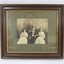 Sepia-toned photograph of John Woodland and his family in a brown wooden frame with a gold bevelled border and grey matt board around the photo. 