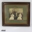 Sepia-toned photograph of John Woodland and his family in a brown wooden frame with a gold bevelled edge and grey matt board around the photo. Black and white 5 cm scale in the foreground.